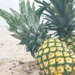 Two whole pineapples resting on sand at the beach, a literal nod to Cloudflare's internal codename Big Pineapple for its DNS platform