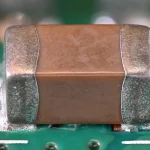 A multilayer ceramic capacitor soldered onto a green circuit board, macro photograph