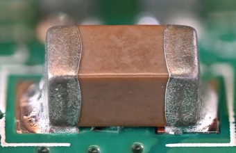 A multilayer ceramic capacitor soldered onto a green circuit board, macro photograph