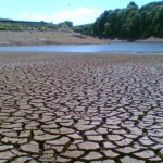 A dried, cracked reservoir bed with a thin strip of remaining water at Holden Wood Reservoir in Lancashire, England, during a drought