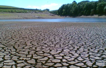 A dried, cracked reservoir bed with a thin strip of remaining water at Holden Wood Reservoir in Lancashire, England, during a drought