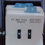 A vintage Rolodex rotary card index filled with handwritten contact cards on a wooden desk