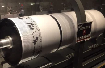 A drum seismograph recording a calm baseline pattern suddenly interrupted by a burst of erratic spikes