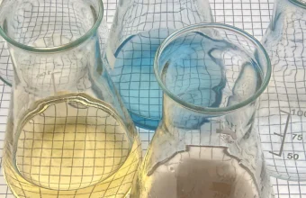 Chemistry lab conical flasks holding colored indicator solutions on a graph-paper background