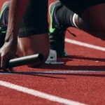 A sprinter's hand gripping a relay baton at the starting blocks on a running track