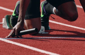 A sprinter's hand gripping a relay baton at the starting blocks on a running track