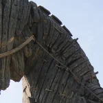 Close-up profile of the wooden Trojan Horse replica at the Canakkale waterfront in Turkey, showing weathered planks and rope bindings against a blue sky