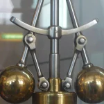 A brass centrifugal flyball governor mechanism used to regulate the speed of a steam engine, displayed in a museum case