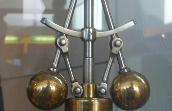 A brass centrifugal flyball governor mechanism used to regulate the speed of a steam engine, displayed in a museum case