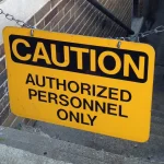 A yellow Caution: Authorized Personnel Only sign hanging from a chain across a brick stairwell