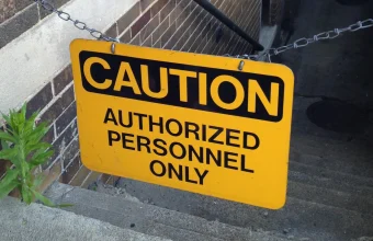 A yellow Caution: Authorized Personnel Only sign hanging from a chain across a brick stairwell