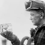 A mine rescue worker in breathing apparatus examines a small canary cage used to detect toxic gas, 1928 U.S. Bureau of Mines photo