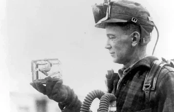 A mine rescue worker in breathing apparatus examines a small canary cage used to detect toxic gas, 1928 U.S. Bureau of Mines photo