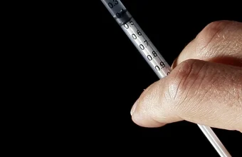 A hand holds a hypodermic syringe with visible dosage markings against a black background, illustrating a SQL injection vulnerability