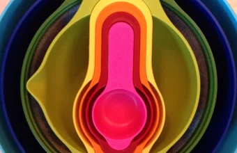 A set of colorful measuring cups and mixing bowls nested one inside another, from largest to smallest, viewed from directly above