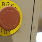 A red industrial emergency stop button on a control panel, illustrating the authority to halt or delay a release