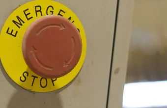 A red industrial emergency stop button on a control panel, illustrating the authority to halt or delay a release