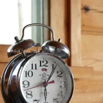 A classic chrome twin-bell alarm clock reading just after 1:30, set against a wood-paneled background