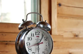 A classic chrome twin-bell alarm clock reading just after 1:30, set against a wood-paneled background