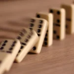 A line of ivory dominoes falling in sequence on a wooden table, one triggering the next