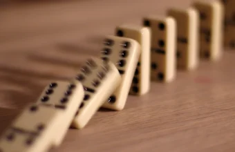 A line of ivory dominoes falling in sequence on a wooden table, one triggering the next