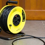 A yellow cable extension reel with its cord unwound across a tiled floor, a visual pun on the malicious browser extension used in the BragJack research. Photo by Sally V, Wikimedia Commons, CC BY-SA 4.0.