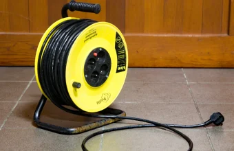 A yellow cable extension reel with its cord unwound across a tiled floor, a visual pun on the malicious browser extension used in the BragJack research. Photo by Sally V, Wikimedia Commons, CC BY-SA 4.0.