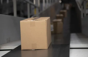 A single cardboard package on a warehouse conveyor belt with more packages queued behind it