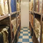 Rows of paper files and folders on metal archive shelves in a narrow storage room
