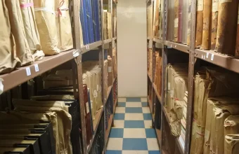 Rows of paper files and folders on metal archive shelves in a narrow storage room