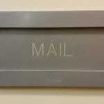 Close-up of a modern gray mail slot engraved with the word MAIL, mounted on an office wall