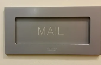 Close-up of a modern gray mail slot engraved with the word MAIL, mounted on an office wall