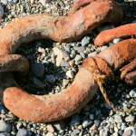 Microsoft’s Humanist AI Code of Conduct Turns Agent Containment Into a Chain of Command A massive rusted anchor chain shackle lying on a pebble beach, its iron surface deeply corroded orange and brown
