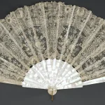 An antique mother-of-pearl and lace folding fan fully spread open against a dark background, a visual metaphor for fanning one query into many