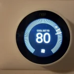 A Google Nest Learning Thermostat mounted on a wall, its display showing a cooling setpoint of 80 degrees