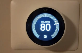 A Google Nest Learning Thermostat mounted on a wall, its display showing a cooling setpoint of 80 degrees