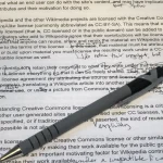 A hand holding a pen mid-edit over a printed page covered in strikethroughs, circled corrections, and handwritten margin notes