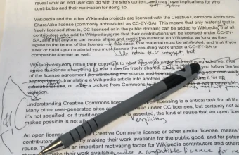 A hand holding a pen mid-edit over a printed page covered in strikethroughs, circled corrections, and handwritten margin notes
