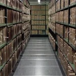 Rows of tied archival document boxes on tall metal shelving stretching down a long storage corridor
