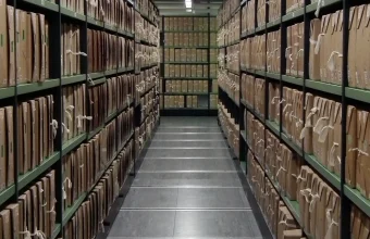 Rows of tied archival document boxes on tall metal shelving stretching down a long storage corridor