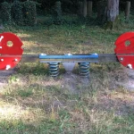 An empty red seesaw balanced on blue springs in a grassy playground, a visual metaphor for a dataset's balance point