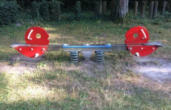 An empty red seesaw balanced on blue springs in a grassy playground, a visual metaphor for a dataset's balance point