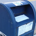 An open USPS mail collection box with a document sitting in the intake slot