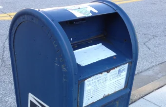An open USPS mail collection box with a document sitting in the intake slot