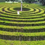 Concentric rings of clipped green hedges forming a circular hedge maze around a central stone pillar in Parque São Roque da Lameira, Porto