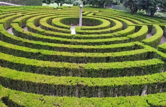 Concentric rings of clipped green hedges forming a circular hedge maze around a central stone pillar in Parque São Roque da Lameira, Porto