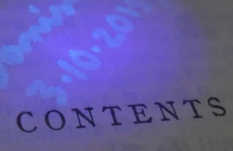 A page of printed text beside handwritten notes that are invisible in normal light but glow under an ultraviolet lamp