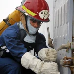 A sailor in damage-control gear closes and dogs down a watertight hatch handle aboard a US Navy ship