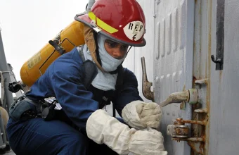 A sailor in damage-control gear closes and dogs down a watertight hatch handle aboard a US Navy ship