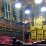 The gilded chamber of the House of Lords at the Palace of Westminster, with red benches and the ceremonial canopy visible
